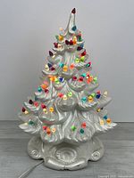Full view of illuminated white ceramic Christmas tree lamp with multicolour bulbs