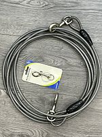 Coiled steel cable with packaged snap hook on grey wood surface