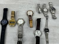 Group view of 11 assorted wrist watches laid out on tabletop