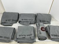 Seven grey “Towel Service” towels spread and folded on surface