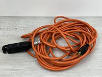 Coiled orange outdoor extension cord showing plug and triple-outlet end