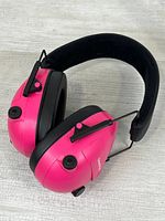Side view of pink earmuffs showing ear cup, control knob, button, headband padding