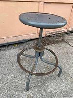 Full view of stool at tallest adjustment showing seat, screw mechanism, foot ring, three legs