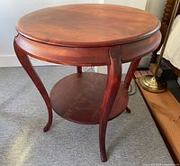 Full view of round hardwood table showing top, legs and shelf