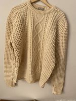 Front view of cream Aran cable-knit sweater on hanger
