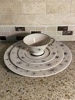 Stacked dinner, salad, bread plates with cup and saucer showing starburst design and gold rim