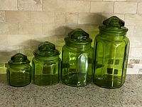Front view of all four graduated green glass canisters with lids