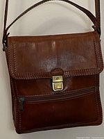 Full front view of brown leather bag showing flap, clasp, zip pocket