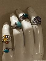 Four rings displayed on mannequin hand: amethyst, two turquoise/chrysoprase, amber multi-stone