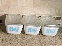 Three Pyrex Butterprint refrigerator dishes with lids displayed side by side