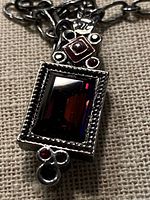 Close-up of pendant front showing red glass stone, accent stones and maker’s tag