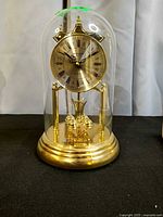 Front view of gold-tone Birks anniversary clock under glass dome showing dial and base