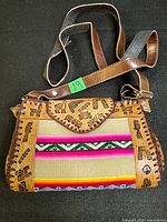 Front view showing tooled leather, woven panel, stamped "CUSCO" flap and strap