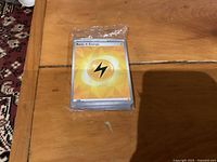 Stack of Pokémon cards sealed in plastic, top Lightning Energy card visible
