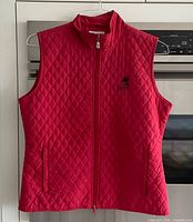 Front view of red quilted vest showing zipper, pockets, logo