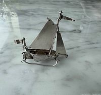Profile view of silver sailboat showing hull, sails, chains, flags