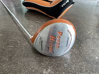 Club head showing Power Hitter branding and weight specs with head cover in background