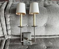 Front view of brushed nickel double sconce with shades on grey upholstered background