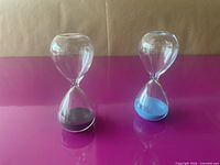 Both hourglasses standing upright showing black and blue sand contents