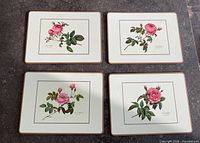 Four matching cream placemats with pink rose illustrations laid out on tabletop showing fronts