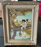 Front view of framed oil painting depicting cows by water, ornate gilt frame visible