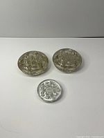 Group view of two large clear glass flower frogs and one small silver-tone metal flower frog