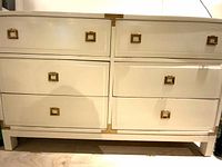 Front view of off-white six-drawer chest with brass pulls and corner brackets