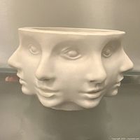Front view of unglazed ceramic bowl showing multiple sculpted faces