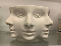 Front view of unglazed white ceramic pedestal bowl with multiple abstract faces