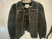 Front view of black quilted jacket on hanger showing trim and buttons