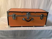 Front view of orange trunk showing latches, handle, chrome trim