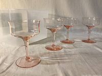 Four of the pink Depression glass sherbet glasses arranged in front of the clear Snapware container, showing shape and color