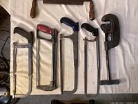 Six cutting tools laid out: four hacksaws, drawknife at top, Ridgid pipe cutter on right