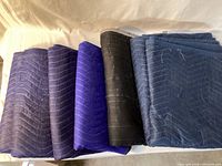 Six folded quilted moving blankets in blue and black displayed side by side
