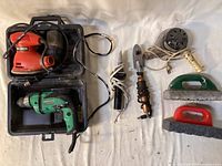 All items laid out: sander in case, drill, two tacking irons, hair dryer, two sanding blocks