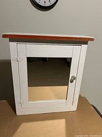Front view of white wooden cabinet with mirrored door and contrasting top