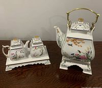 Front view of entire porcelain tea set showing teapot on stand, creamer and sugar on tray