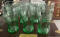 Six of the seven green Coca-Cola tumblers on display, showing embossed logos and heavy bases