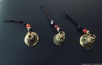 Three gold-tone brass Feng Shui bells with cords and beads, front view