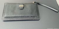 Front view of black Kate Spade wristlet with strap and exterior pocket