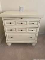 Front view showing cream bedside table with three drawers and bun feet
