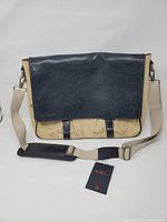 Front view of beige canvas messenger with navy leather flap and tag attached
