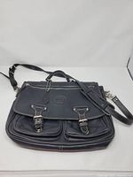 Front view showing leather satchel, buckle pockets, strap