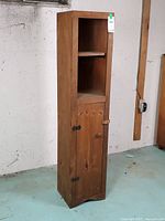 Full front view of tall narrow wooden cupboard showing open shelves and lower door