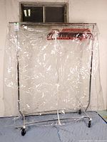 Full view of metal rolling garment rack with clear cover and hangers