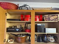 Overall view of open cabinet showing coffee makers, carafes, canisters, boxed items, cookware, baskets