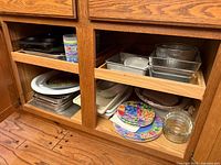 Cabinet showing top pull-out shelf with glass baking dishes, metal pans and tumbler