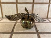 Front view of brass apple sculpture with leaves displayed on tile surface