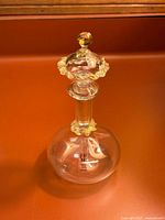 Full view of round clear glass perfume bottle with gold leaf stopper and neck trim