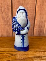 Front view of blue and white salt-glazed stoneware Santa figurine holding tree